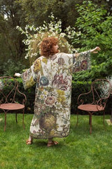 Woman in a floral dress standing in a garden with chairs and flowers.