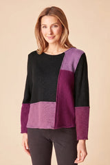 Woman wearing a plum, purple and black color-blocked sweater on a beige background