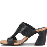 A black leather slide sandal with a chunky block heel and a tan insole, shown from a side profile view against a white background.