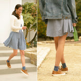 Woman wearing a blue checkered dress with a denim jacket and brown shoes, standing on steps.