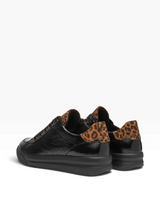 A pair of black leather low-top sneakers with brown and black leopard print heel tabs, shown from a three-quarters angle on a white background.