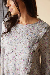 Close up of a woman wearing a knit sweater with a row of buttons on the left side