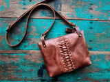 Brown leather handbag with woven detail on a rustic wooden surface