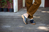 Person wearing black clogs on a wooden floor with plants in the background