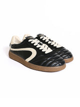 A pair of black leather low-top sneakers with cream-colored side stripes, cream laces, and brown gum soles, displayed on a clean white background.