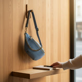 Blue leather medium sling bag with antique bronze chain detail and adjustable strap, used to store a phone.