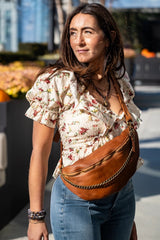 Strada brown leather sling bag with antique bronze chain detail, worn by a woman in a floral top and jeans.