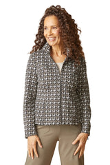 A smiling woman with long curly brown hair models a zip-up jacket featuring a black and white houndstooth pattern, paired with tan pants, against a solid white background.