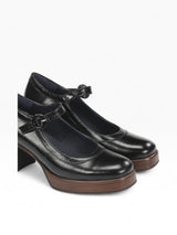 Pair of black leather shoes with brown soles on a light gray background
