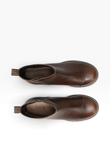 A pair of dark brown leather ankle boots shown from a top-down view on a white background. The boots feature a side zipper, contrast stitching, and a pull tab with the brand name 'taos' visible.