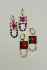 Pair of earrings with square designs and gemstone accents on a light gray background