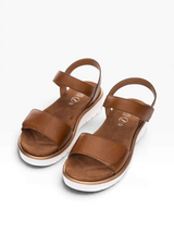 A pair of brown leather slide sandals with wide straps and a low wedge heel, displayed on a clean white background.