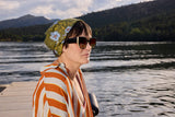Woman wearing sunglasses and a patterned headscarf by a lake with mountains in the background