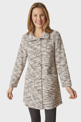A woman modeling a long-sleeve, knee-length tweed coat with a textured black and beige pattern, featuring a notched collar and front buttons, set against a solid light gray background.
