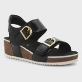 A black wedge sandal with two wide straps, gold-tone buckle details, and a cork-textured wedge heel on a light gray background.