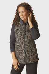 A woman modeling a sleeveless zip-front vest with a brown and black leopard print pattern over a black long-sleeve shirt, against a light gray studio background.
