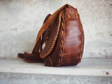 Brown leather bag with intricate stitching on a light gray background