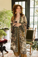 Woman in a floral robe holding a glass of wine in a decorated room.