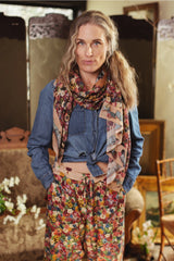 Woman wearing a blue shirt, floral scarf, and colorful pants in an indoor setting.