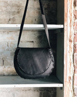 Black leather handbag with a strap on a metal shelf against a rustic wall.