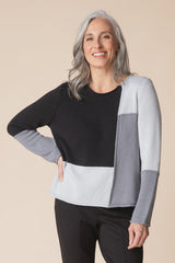 Woman wearing a black, gray, and white color-blocked sweater on a beige background