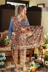 Woman holding a floral-patterned shawl with bear design in a home setting.