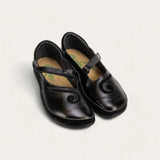 A pair of black leather Mary Jane shoes with hook-and-loop straps and decorative swirl details on the vamp, shown on a light cream background. The brand name 'Kiko Kiko' is visible on the tan insoles.