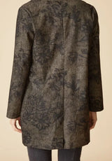 Back of a woman wearing a black floral pattern on an umber colored car coat