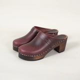 Pair of redish brown leather clogs on a light beige background