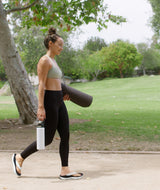 Woman walking with a yoga mat and water bottle in a park