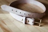 Ivory leather belt with a brass buckle on a wooden surface