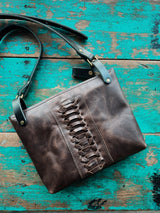 Brown leather bag with decorative cut-out details on a rustic wooden surface