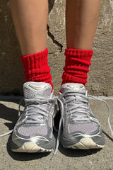 Gray sneakers with red socks worn against a stone wall.