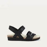Black sandal with criss-cross straps on a light beige background