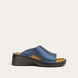 A single women's slide sandal with a metallic blue leather upper and a chunky black wedge heel, shown from a side profile against a light off-white background.