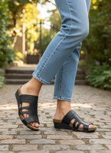 Strada Naot Carriage black leather wedge slide sandals with cutout details and cork footbed worn with blue jeans.